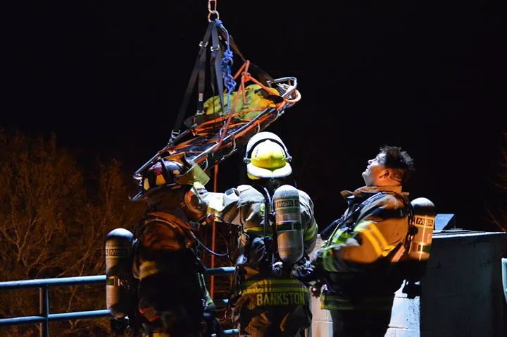 Firefighters performing technical rope rescue with Stokes basket at night